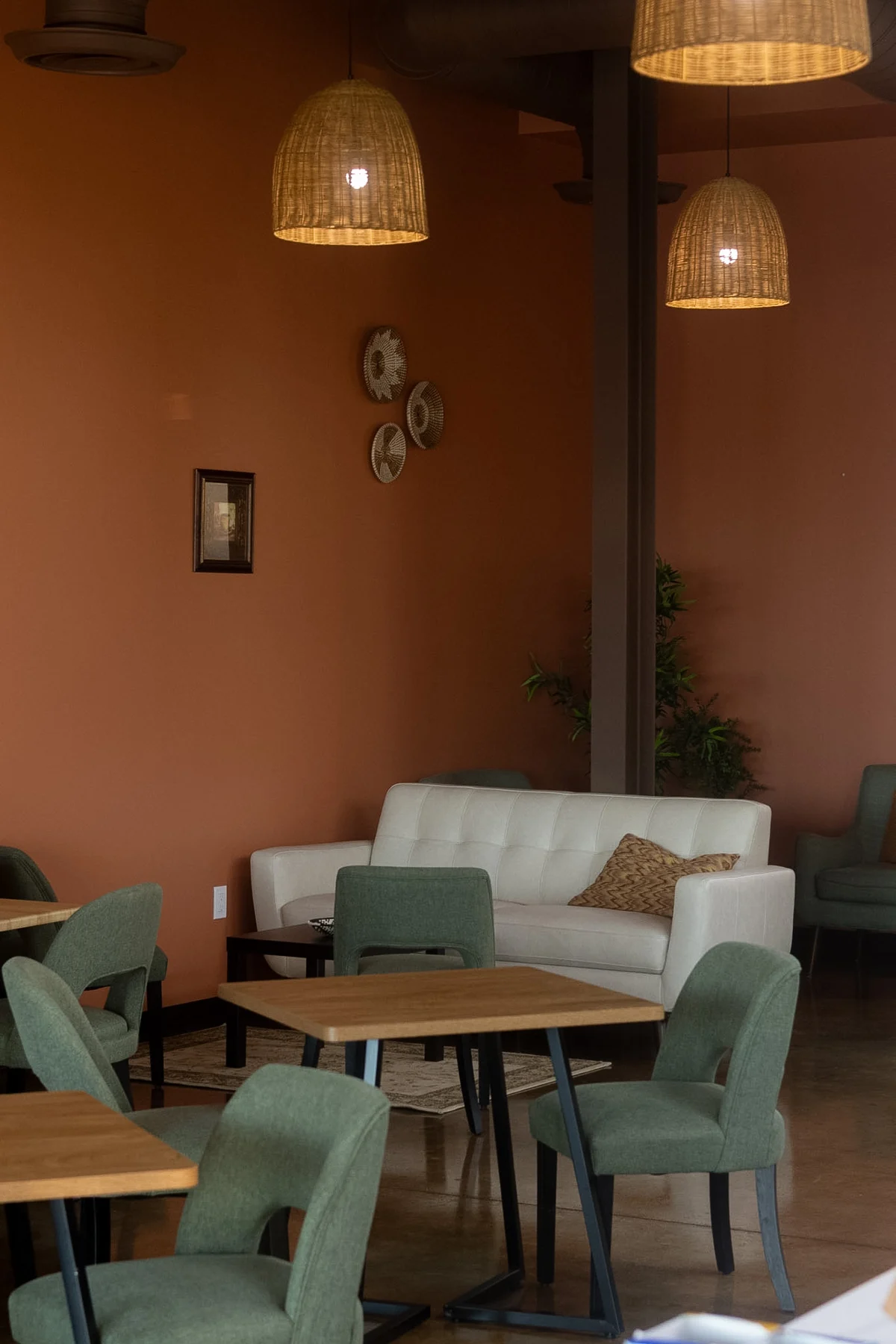 Elura’s lounge with sage green chairs, warm terracotta walls, and woven pendant lights
