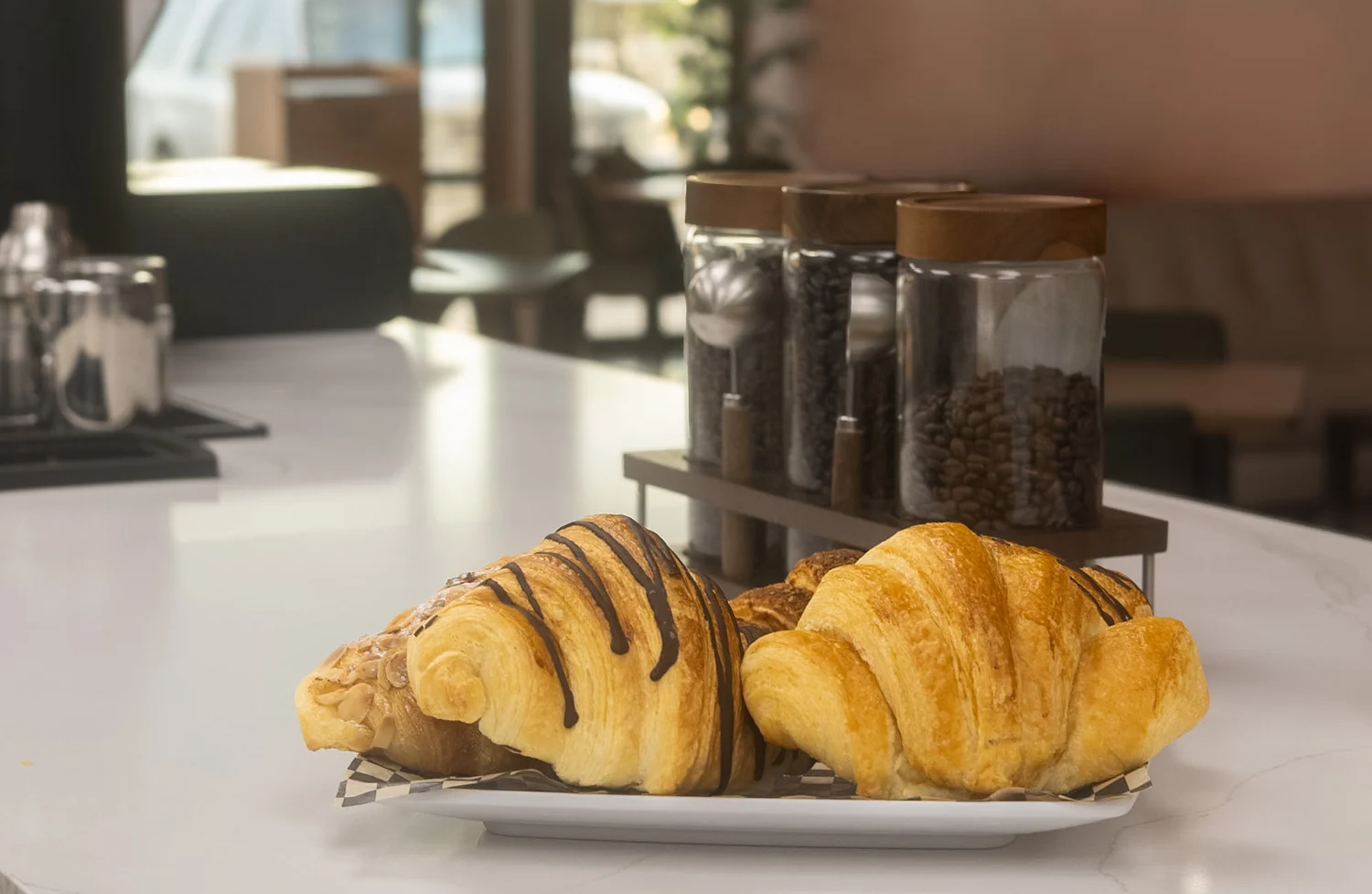 Two golden croissants, one with a chocolate drizzle, served together on a plate